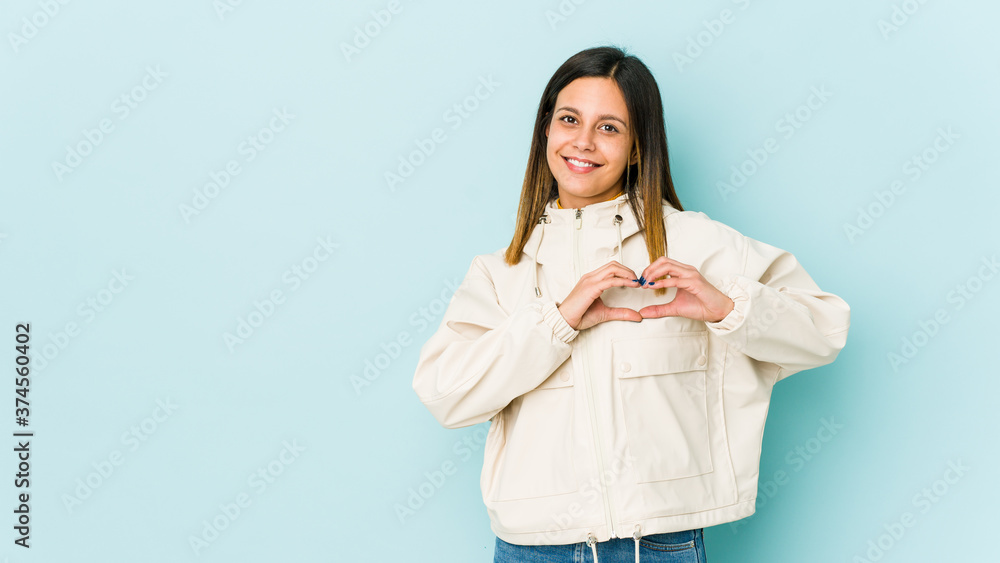 Young woman isolated on blue background smiling and showing a heart shape with hands. Young woman isolated on blue background smiling and showing a heart shape with hands.