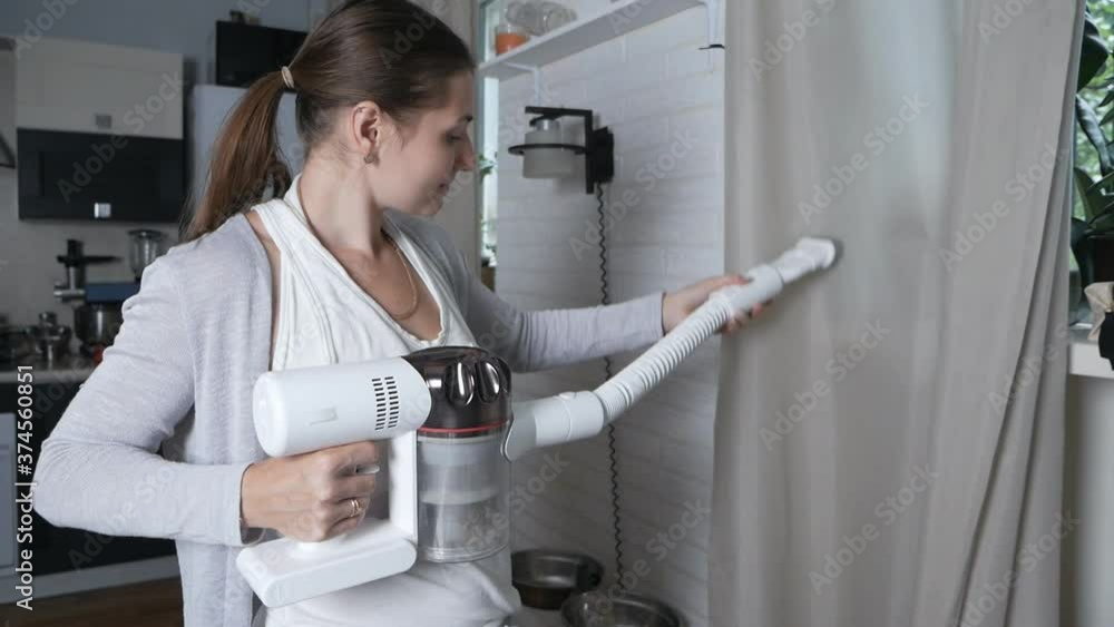 Close-up of the head of a modern vacuum cleaner removing dust from a curtain. Home cleaning concept. Woman cleans curtains with professional equipment in the room Close-up of the head of a modern vacuum cleaner removing dust from a curtain. Home cleaning concept. Woman cleans curtains with professional equipment in the room