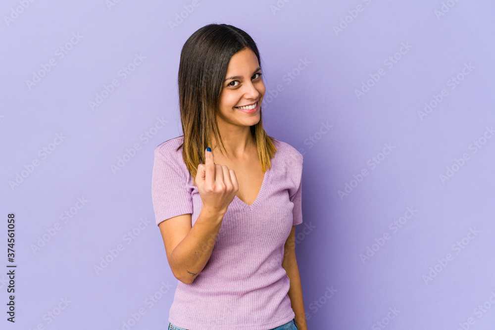 Young woman isolated on purple background pointing with finger at you as if inviting come closer. Young woman isolated on purple background pointing with finger at you as if inviting come closer.
