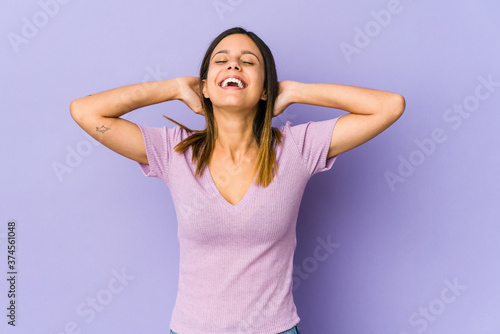 Young woman isolated on purple background feeling confident, with hands behind the head.