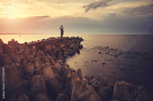 Pier with lighthouse protected by breakwater tetrapods at sunset, color toning applied.