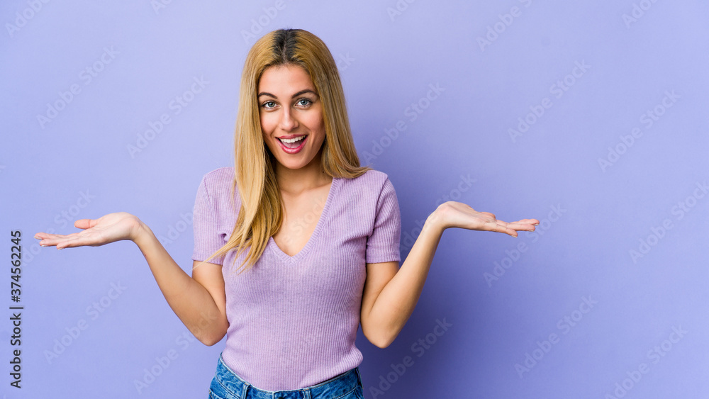 Young blonde woman isolated on purple background showing a welcome expression. Young blonde woman isolated on purple background showing a welcome expression.