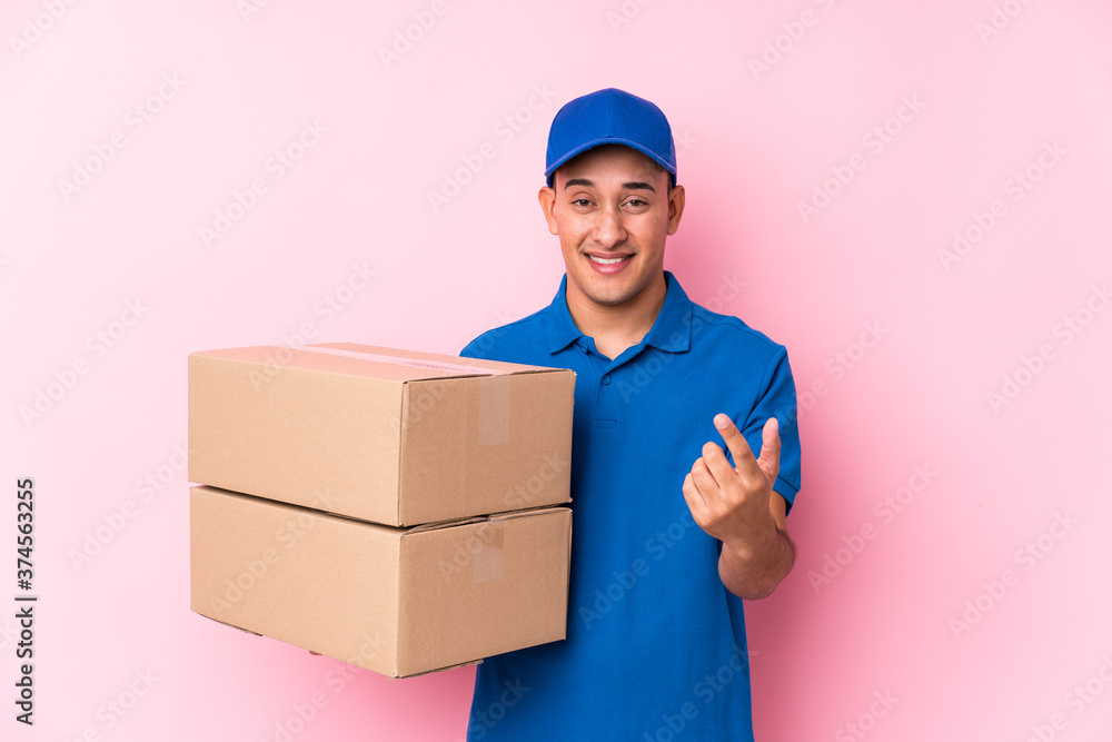 Young latin delivery man isolated pointing with finger at you as if inviting come closer. Young latin delivery man isolated pointing with finger at you as if inviting come closer.