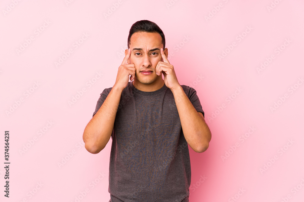Yooung latin man posing in a pink backgroundfocused on a task, keeping forefingers pointing head. Yooung latin man posing in a pink backgroundfocused on a task, keeping forefingers pointing head.