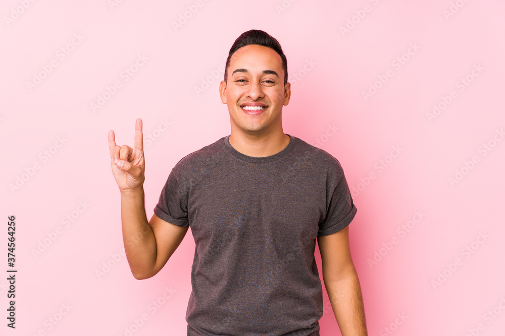 Yooung latin man posing in a pink backgroundshowing a horns gesture as a revolution concept. Yooung latin man posing in a pink backgroundshowing a horns gesture as a revolution concept.
