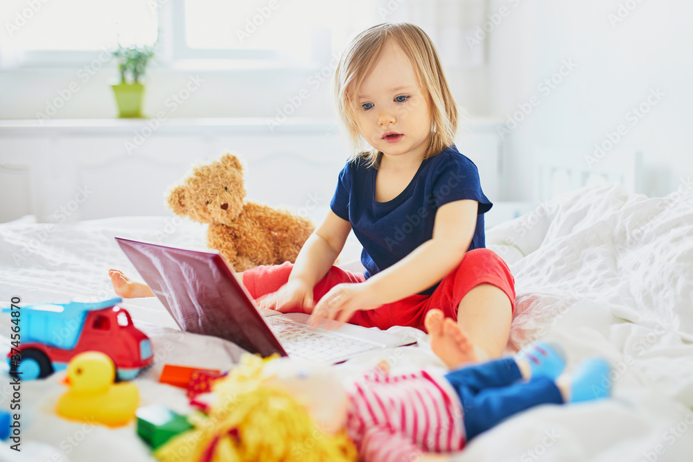 Toddler girl with laptop and toys in bed Toddler girl with laptop and toys in bed