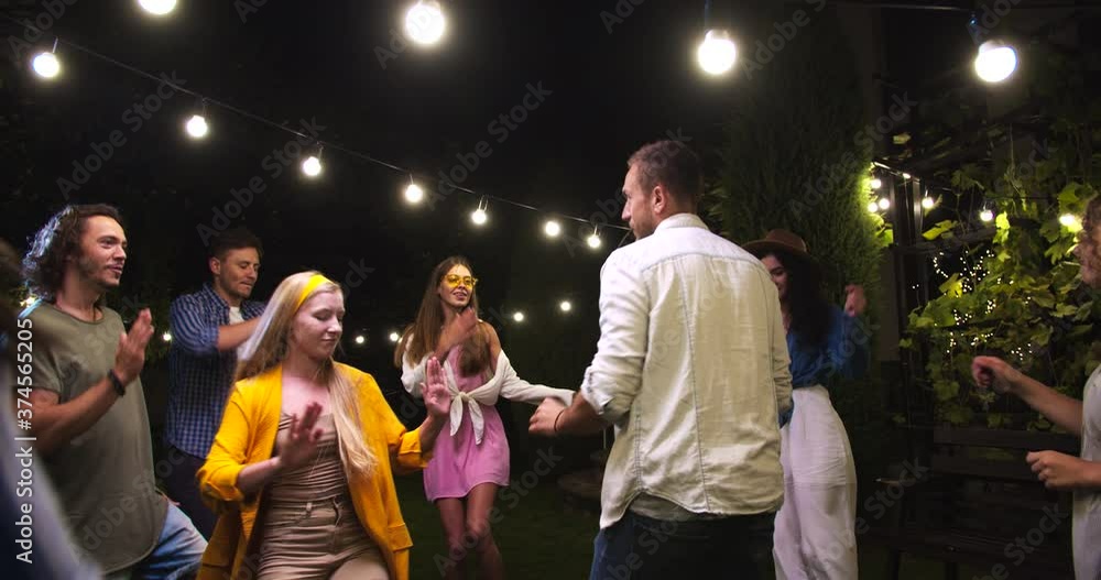 Cheerful young Caucasian males and females moving to music at garden party in good mood. Beautiful girls and handsome boys having fun and dancing. Party celebration at night. Outdoors concept Cheerful young Caucasian males and females moving to music at garden party in good mood. Beautiful girls and handsome boys having fun and dancing. Party celebration at night. Outdoors concept