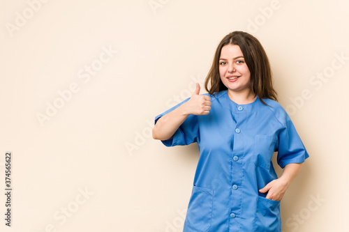 Young curvy nurse woman smiling and raising thumb up