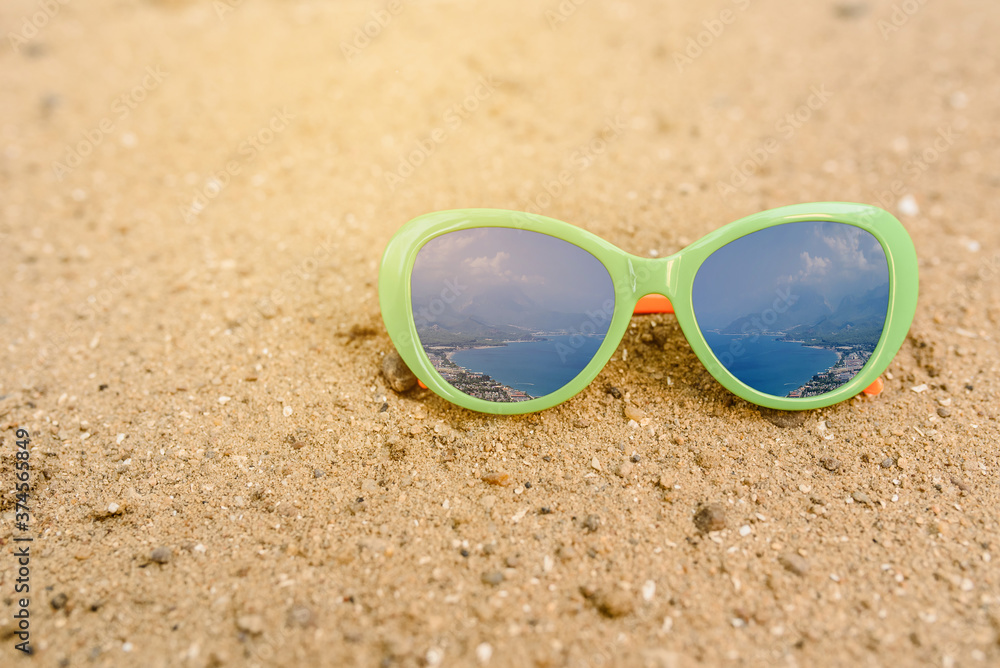 Close up sunglasses on the sand with  sea and sky reflection in it.