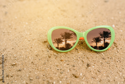 Close up sunglasses on the sand with palms reflection in it.