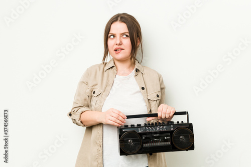 Young curvy woman holding a retro radio confused, feels doubtful and unsure.