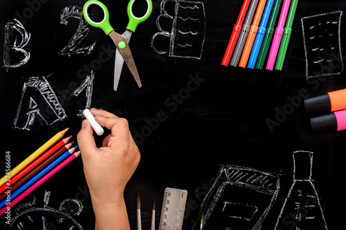 Student hand with chalk is drawing digits and letters on the school blackboard.