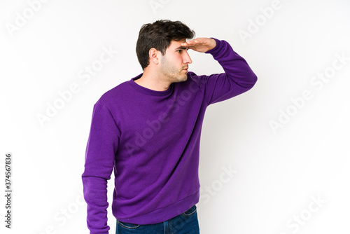 Young man isolated on white background looking far away keeping hand on forehead.