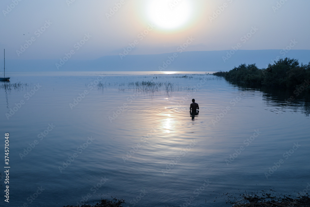 Man dipped in the water of Galilee Lake in Israel at sunrise.