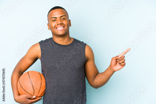 Young colombian man playing basketball isolated smiling and pointing aside, showing something at blank space. © Asier