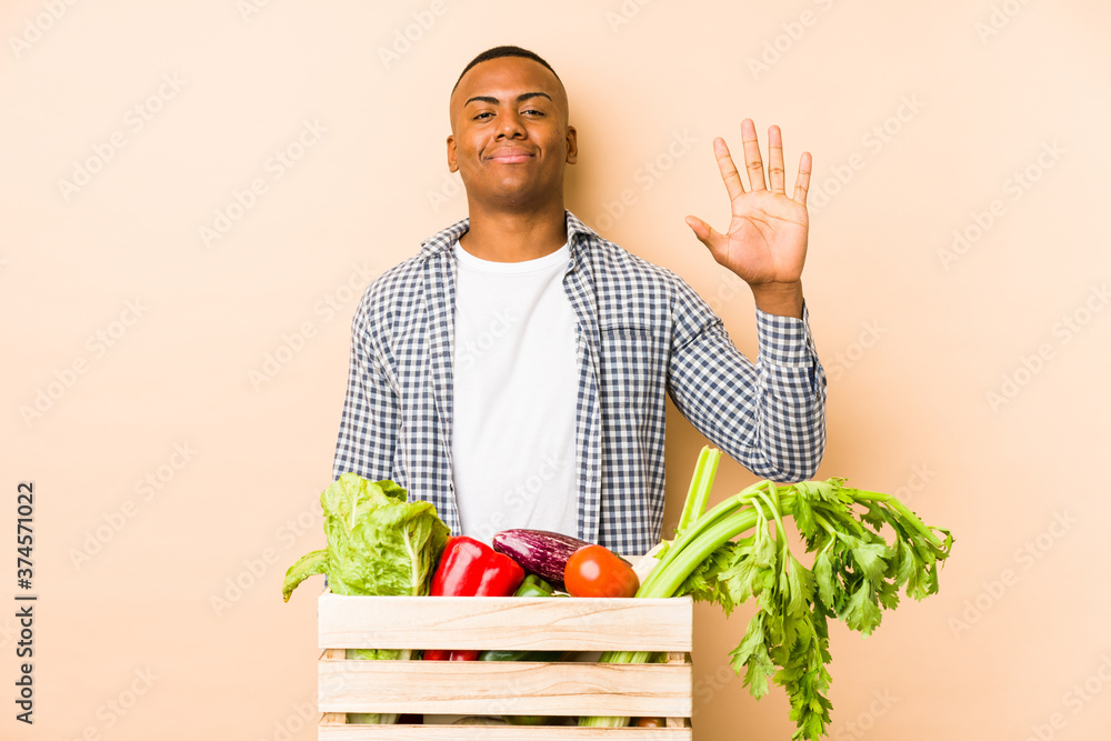 Young farmer man isolated on a beige background smiling cheerful showing number five with fingers. Young farmer man isolated on a beige background smiling cheerful showing number five with fingers.