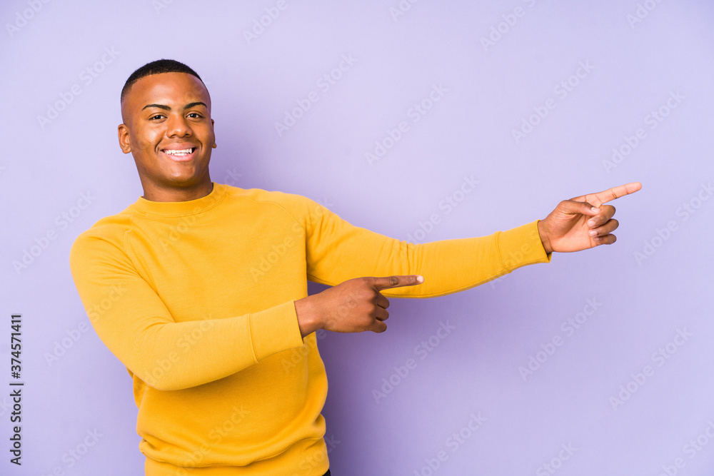 Young latin man isolated on purple background excited pointing with forefingers away. Young latin man isolated on purple background excited pointing with forefingers away.
