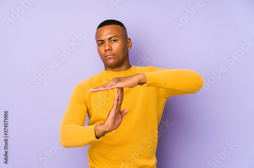 Young latin man isolated on purple background showing a timeout gesture.