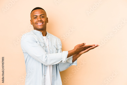 Young latin man isolated on beige background holding a copy space on a palm.