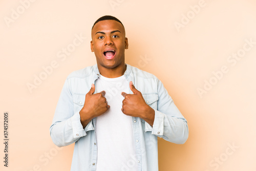 Young latin man isolated on beige background surprised pointing with finger, smiling broadly.