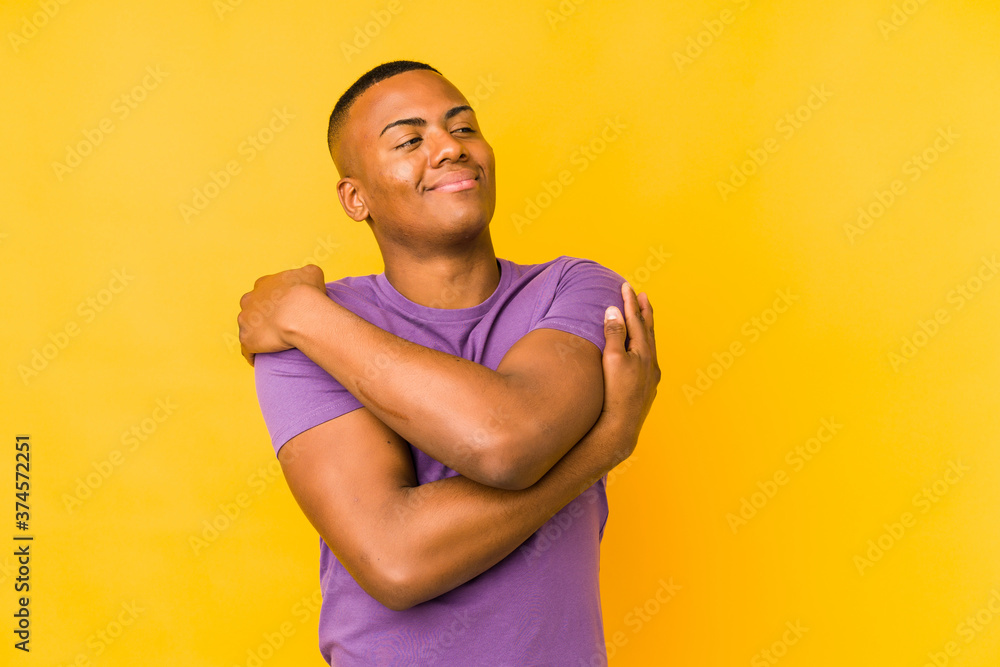 Young latin man isolated on yellow background hugs, smiling carefree and happy.