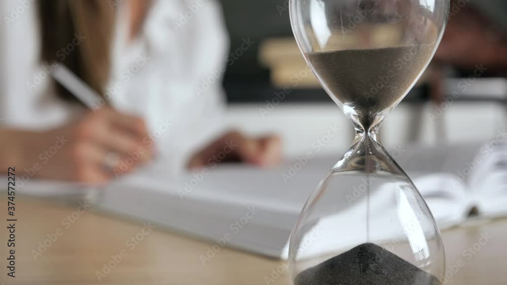 close-up hourglass. Silhouette woman reading a book and write conspectus on a blurred background 4k close-up hourglass. Silhouette woman reading a book and write conspectus on a blurred background 4k
