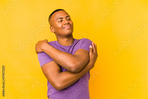 Young latin man isolated on yellow background hugs, smiling carefree and happy.