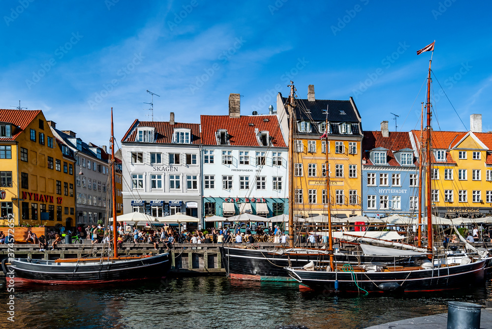 Scenic summer view of the must-see Nyhavn pier in Copenhagen, with people having relax, colorful buildings and boats.