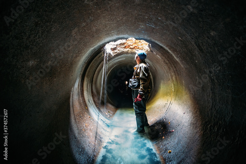 Sewer tunnel worker examines sewer system damage and wastewater leakage photo