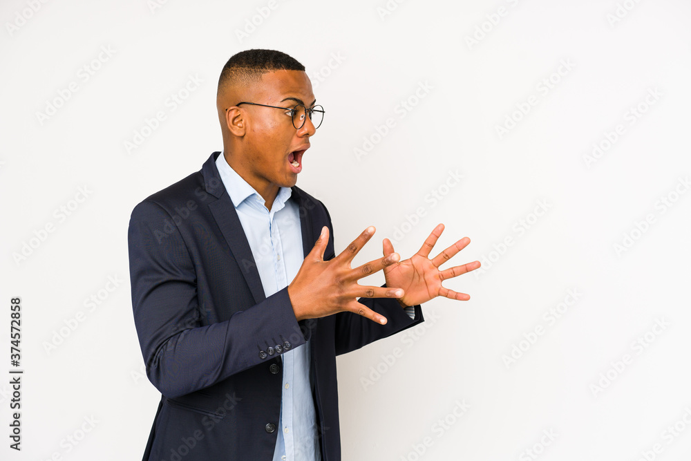 Young business latin man isolated on white background shouts loud, keeps eyes opened and hands tense. Young business latin man isolated on white background shouts loud, keeps eyes opened and hands tense.