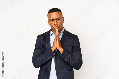 Young business latin man isolated on white background holding hands in pray near mouth, feels confident.