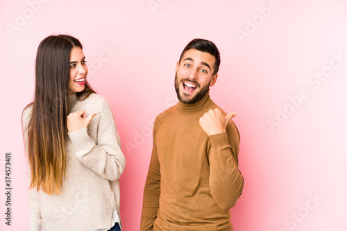 Young caucasian couple isolated points with thumb finger away, laughing and carefree.