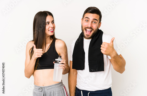 Young caucasian fitness couple isolated raising both thumbs up, smiling and confident.