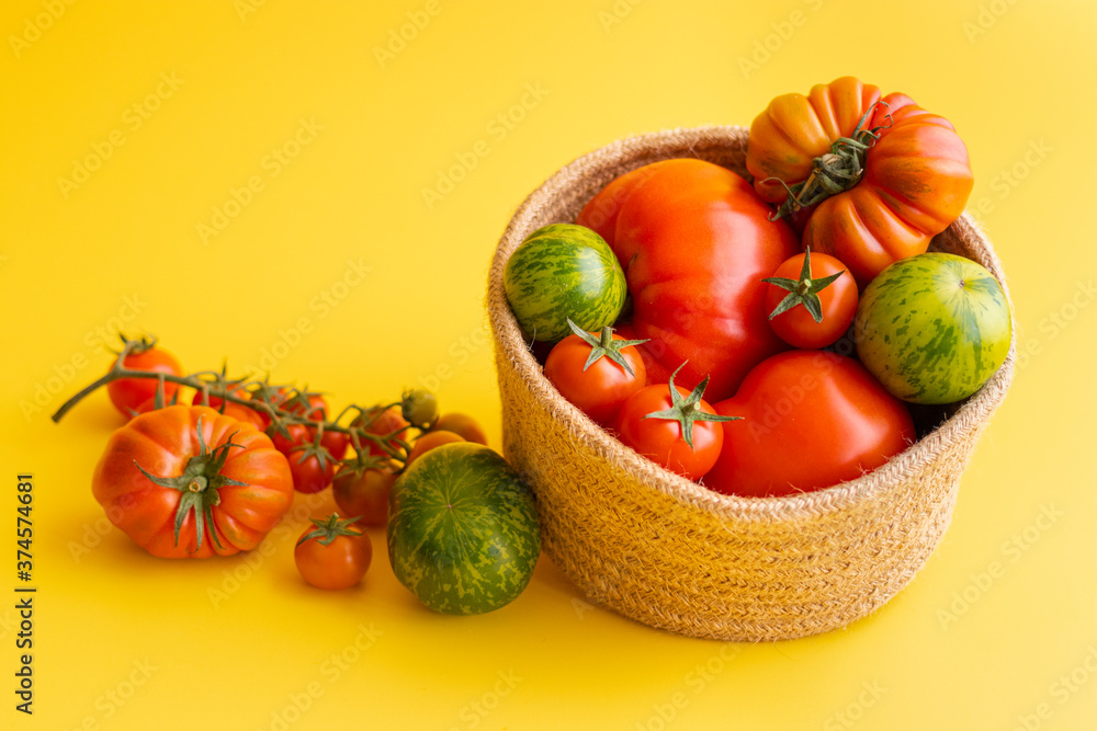 Basket with a variety of tomatoes, including: Cherry, Heirloom and Zebra on a yellow background Basket with a variety of tomatoes, including: Cherry, Heirloom and Zebra on a yellow background