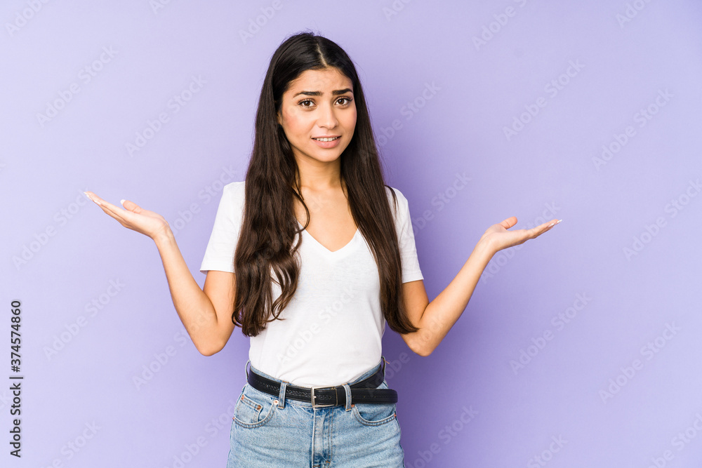 Young indian woman isolated on purple background confused and doubtful shrugging shoulders to hold a copy space. Young indian woman isolated on purple background confused and doubtful shrugging shoulders to hold a copy space.