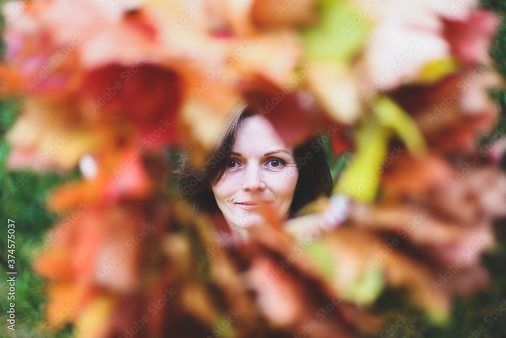 Brunette caucasian happy woman in circle frame of maple leaves wreath. Autumn harvest, nature concept. Flowers bouquet of orange, red, yellow leaves. Park, garden, forest fall photo shoot