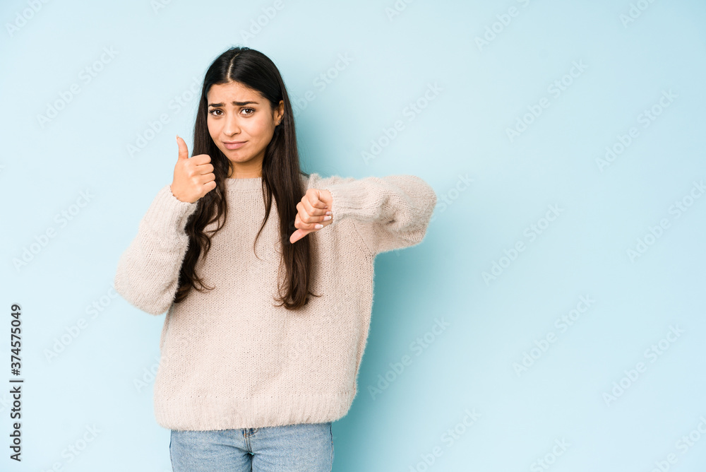 Young indian woman isolated on blue background showing thumbs up and thumbs down, difficult choose concept Young indian woman isolated on blue background showing thumbs up and thumbs down, difficult choose concept