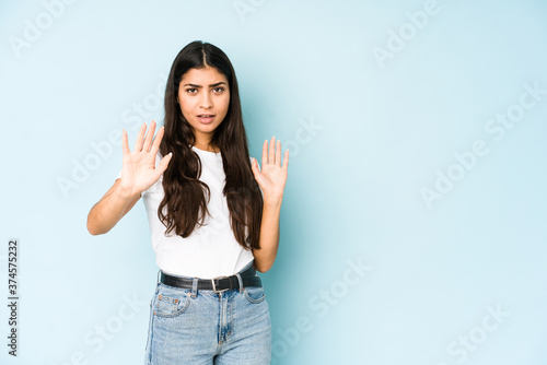 Young indian woman on blue background being shocked due to an imminent danger