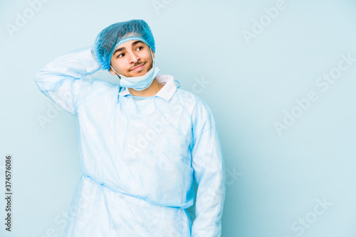 Young arabian surgeon man isolated against on a blue background touching back of head, thinking and making a choice. © Asier
