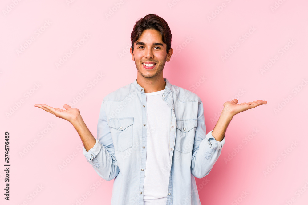 Young caucasian man posing in a pink background isolated makes scale with arms, feels happy and confident. Young caucasian man posing in a pink background isolated makes scale with arms, feels happy and confident.