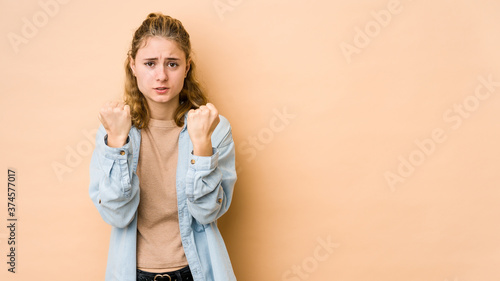 Young caucasian woman isolated on beige background showing fist to camera, aggressive facial expression.