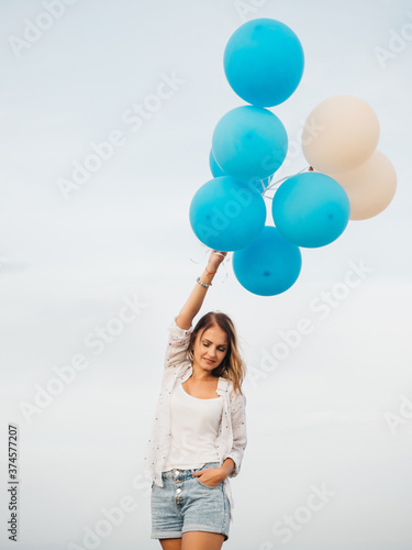 Young woman holding blue and white helium balloons