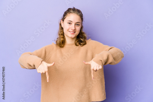Young caucasian woman on purple background points down with fingers, positive feeling.