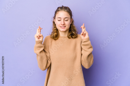 Young caucasian woman on purple background crossing fingers for having luck