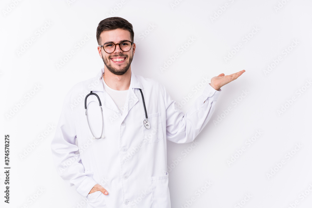 Young caucasian doctor man isolated showing a copy space on a palm and holding another hand on waist. Young caucasian doctor man isolated showing a copy space on a palm and holding another hand on waist.