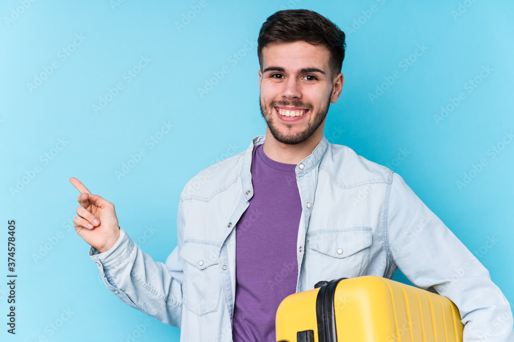 Young caucasian traveler man holding a suitcase isolated smiling and pointing aside, showing something at blank space. Young caucasian traveler man holding a suitcase isolated smiling and pointing aside, showing something at blank space.