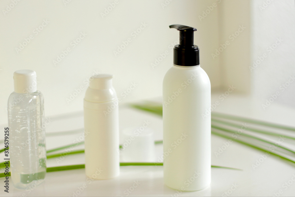 Face/body care concept: bottles of creams/lotions/serums, white plastic jar with green leaves on background Face/body care concept: bottles of creams/lotions/serums, white plastic jar with green leaves on background