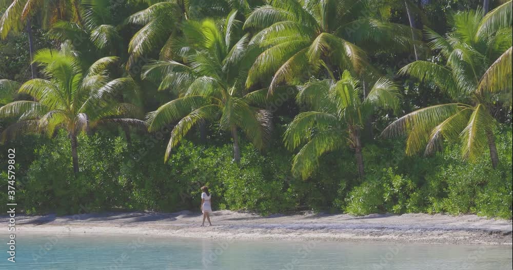 Woman wearing Tahiti flower crown walks on lush, tropical beach near