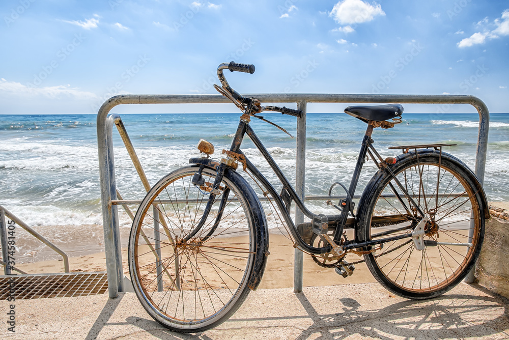 Old retro style bike parked on a sandy beach on a backgrouns of blue sea
