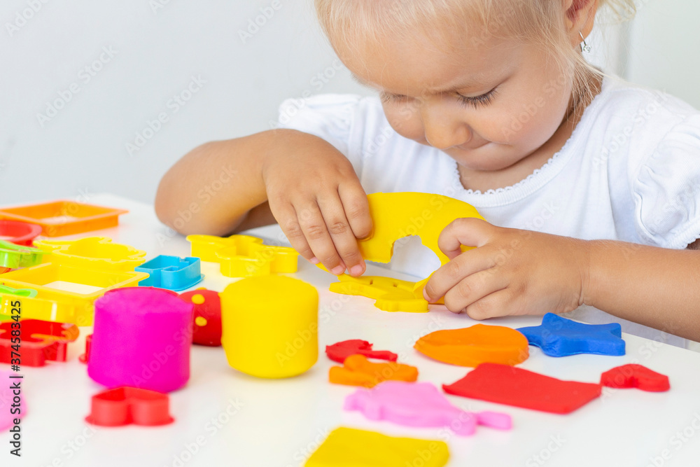 Toddler sculpts from colored plasticine on a white table. The hand of a small child squeezes pieces of colored plasticine. Childrens creativity, educational games, fine motor skills Toddler sculpts from colored plasticine on a white table. The hand of a small child squeezes pieces of colored plasticine. Childrens creativity, educational games, fine motor skills